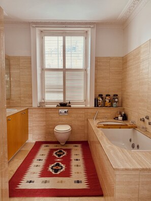 A bathroom with a toilet, sink, bathtub, and a window with blinds.