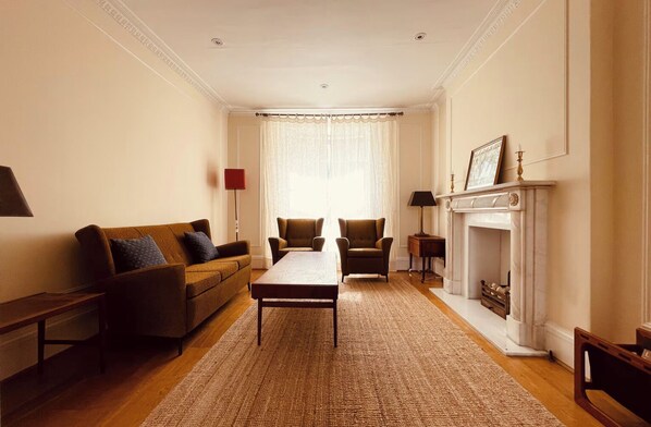 A living room with a sofa, chairs, a table, a fireplace, and a window with curtains.