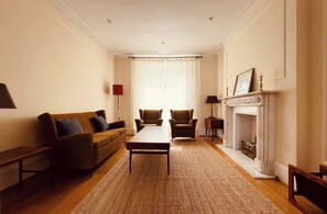 A living room with a sofa, chairs, a table, a fireplace, and a window with curtains.