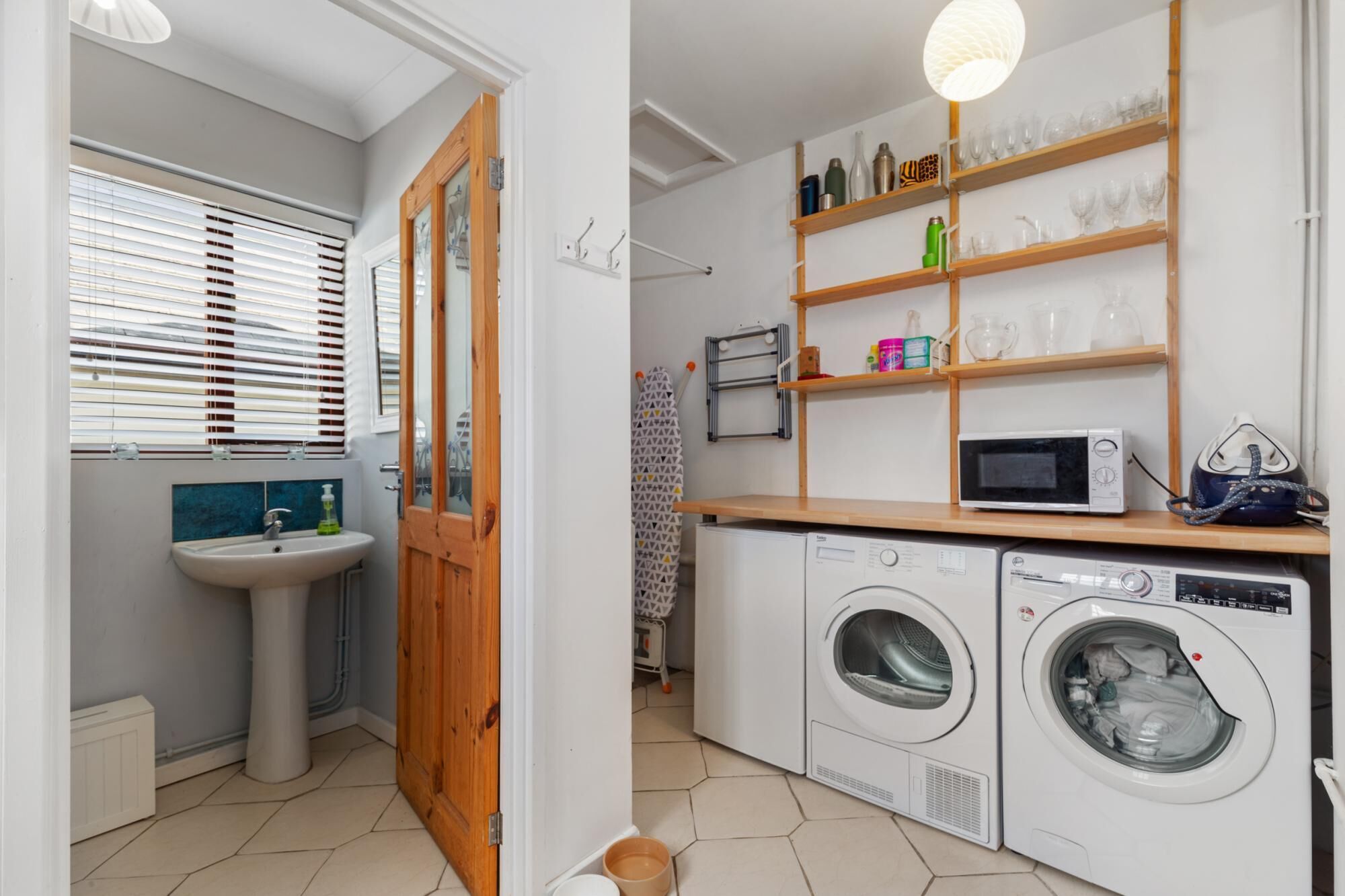 A laundry area with a washing machine, dryer, and shelves with glassware and bottles.