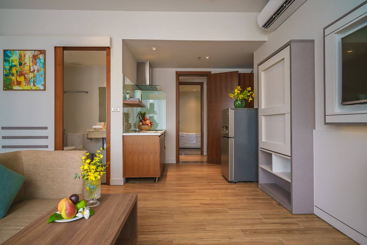 Una cocina moderna con refrigerador, un mueble de madera y una encimera. Hay un comedor con mesa y sillas.