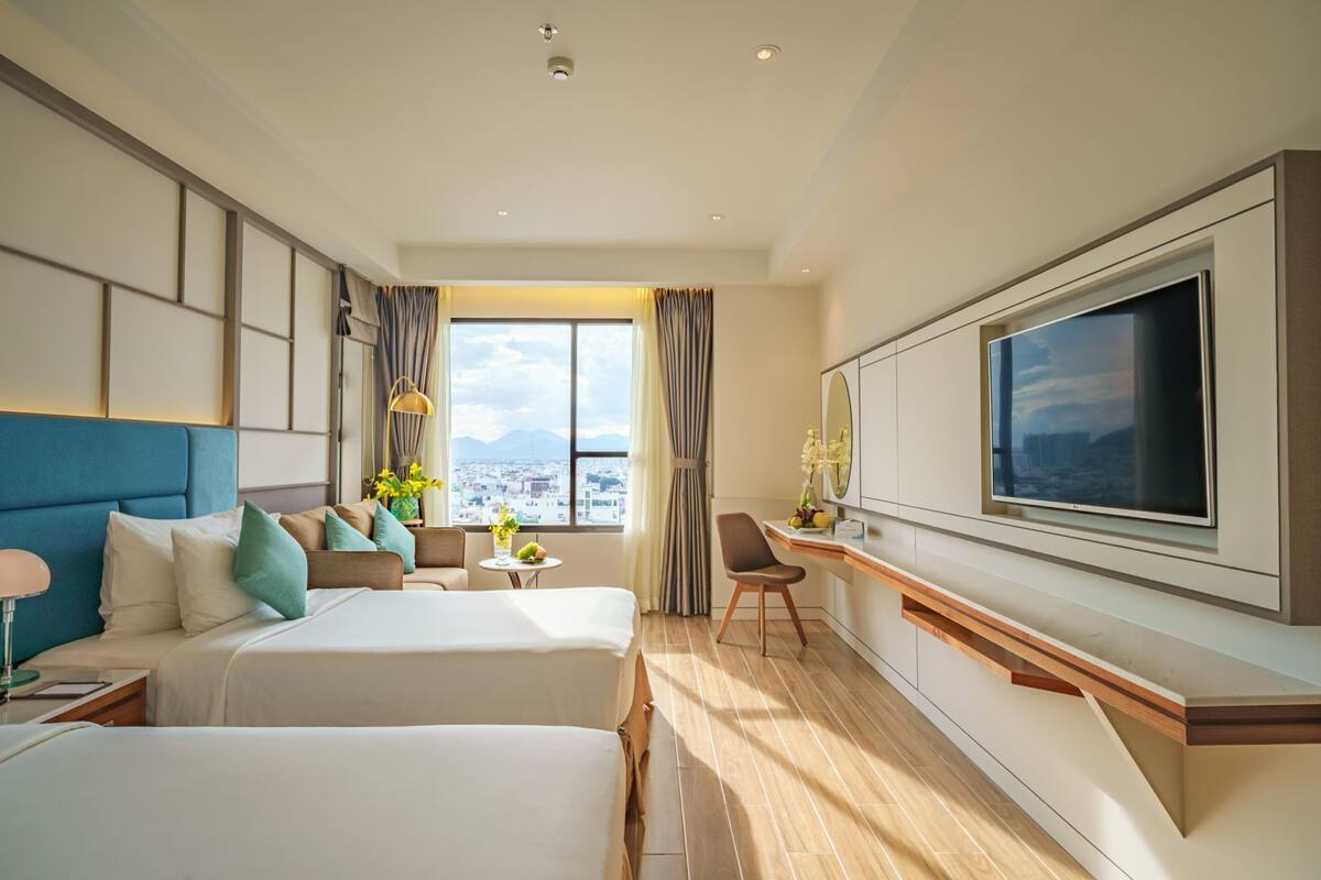 Habitación de hotel con dos camas, un escritorio, un televisor y vistas a la ciudad.