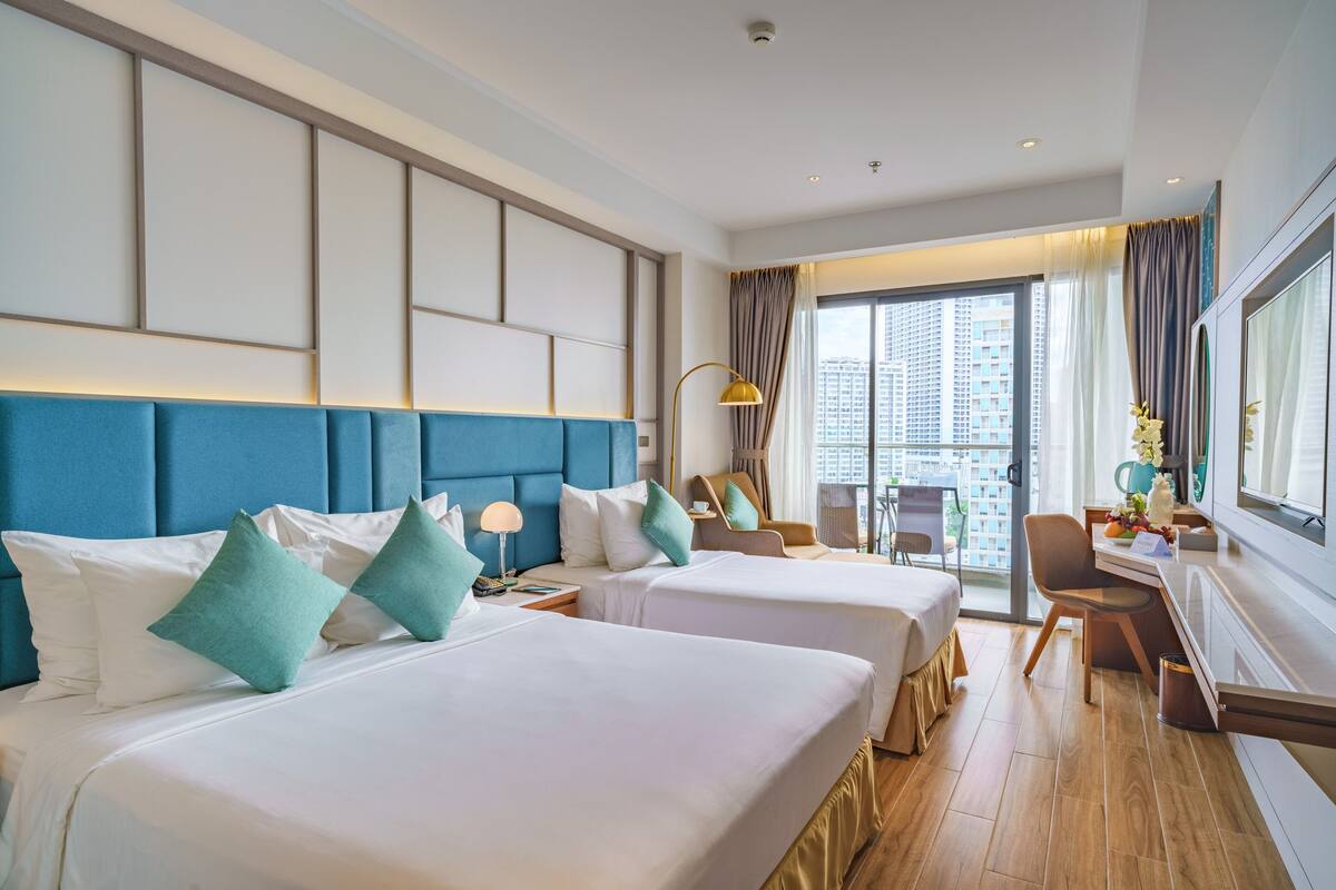 Habitación de hotel con dos camas, un escritorio y un amplio ventanal con vistas a la ciudad.