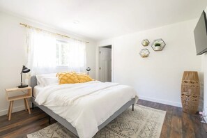 Un dormitorio con cama, mesita de noche, lámpara, alfombra y televisión instalada en la pared.