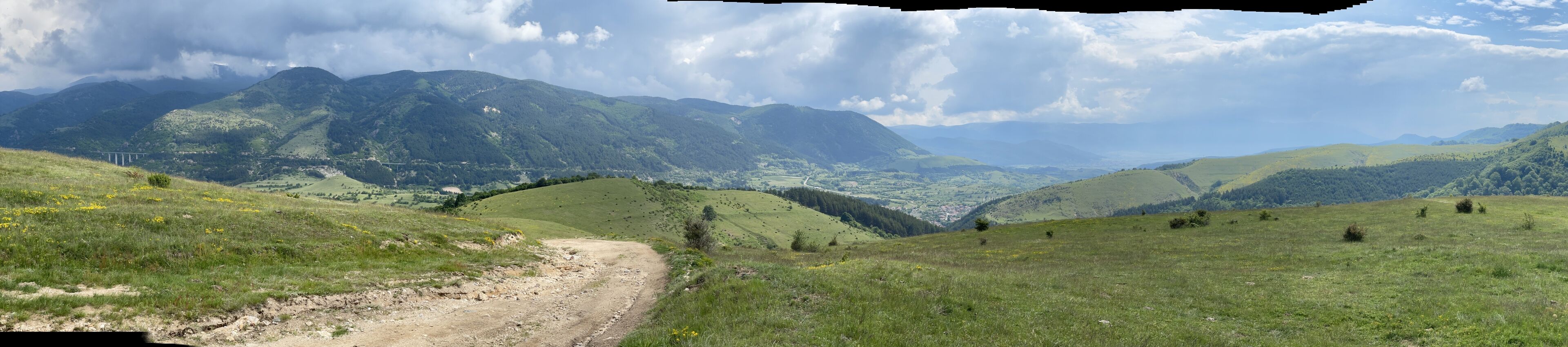 Paisaje rural con un camino de tierra que serpentea entre colinas onduladas y montañas al fondo.