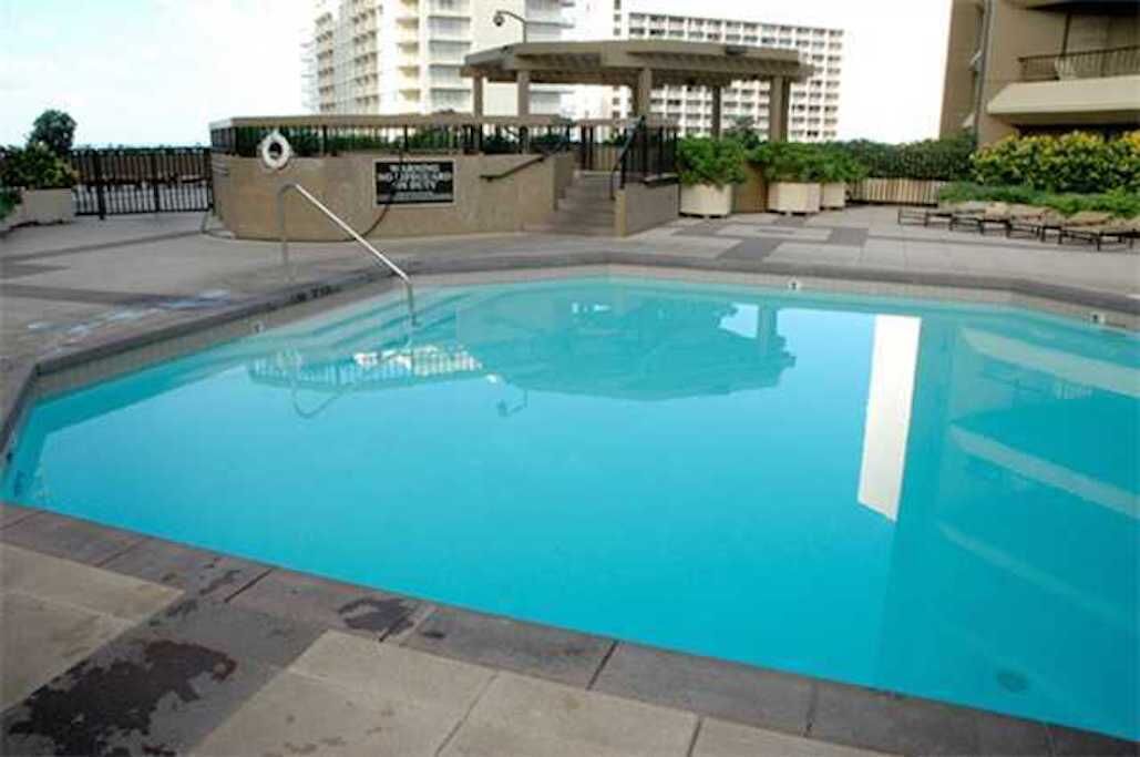 A swimming pool with a clear blue water, surrounded by a paved deck and a gazebo.
