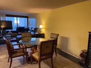 Uma sala de estar com uma mesa de jantar, cadeiras, um sofá, uma televisão e um abajur.