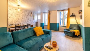 Un salon chaleureux avec un canapé de couleur turquoise, une petite table ronde sur laquelle repose une télécommande, et une fenêtre agrémentée de rideaux.