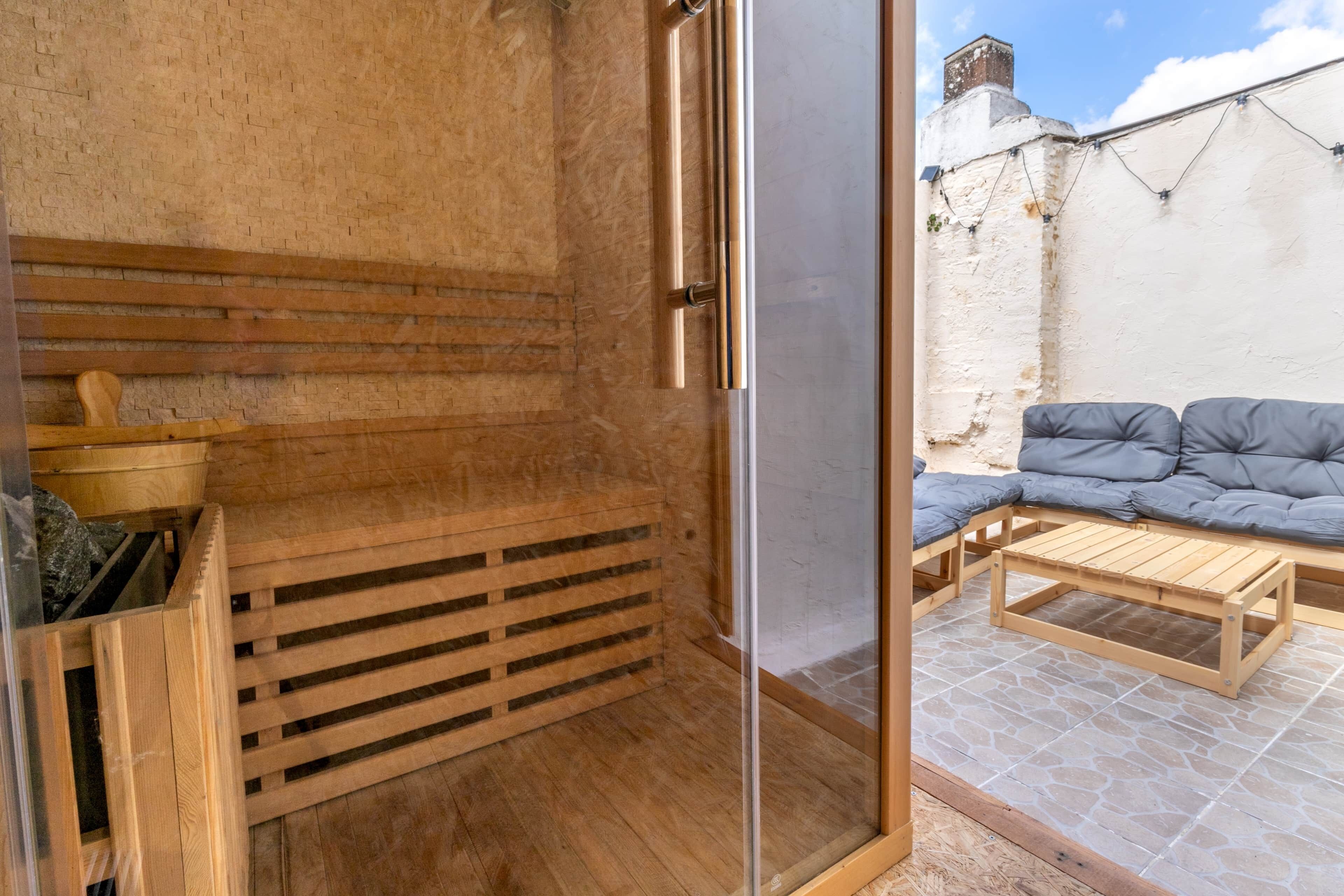 A wooden interior with a glass door leading to an outdoor seating area with a cushioned bench and a wooden table.