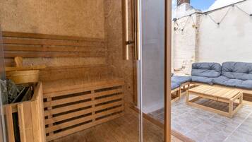 A wooden interior with a glass door leading to an outdoor seating area with a cushioned bench and a wooden table.