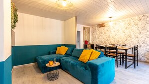 Un salon moderne avec des canapés de couleur turquoise, une table basse ronde et un coin repas comprenant une table et des chaises en bois.