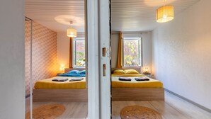 Une chambre avec deux lits, un plancher en bois et une grande fenêtre.