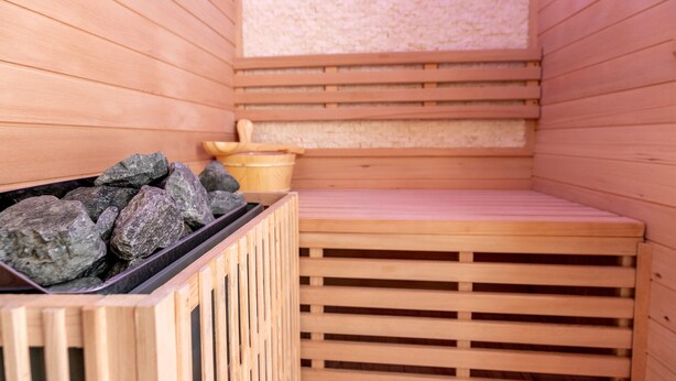 Un sauna en bois avec un banc, un récipient rempli de pierres et un seau en bois.