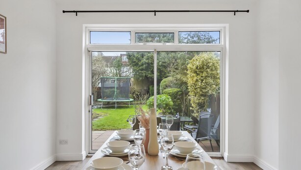 A dining area with a table set for six, a vase, and a view of a garden through a sliding glass door. - BIG House Free Parking Walking Distance to Kensal Rise Station (London)