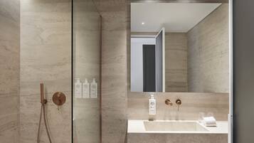 A modern bathroom with a glass-enclosed shower, a large mirror, and a vanity with a sink and toiletries.