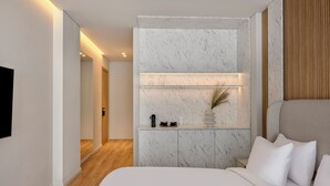 A modern bedroom with a large bed, a built-in shelf with glassware, and a wooden panel wall. - Nur Aparthotel Athens (Athens)