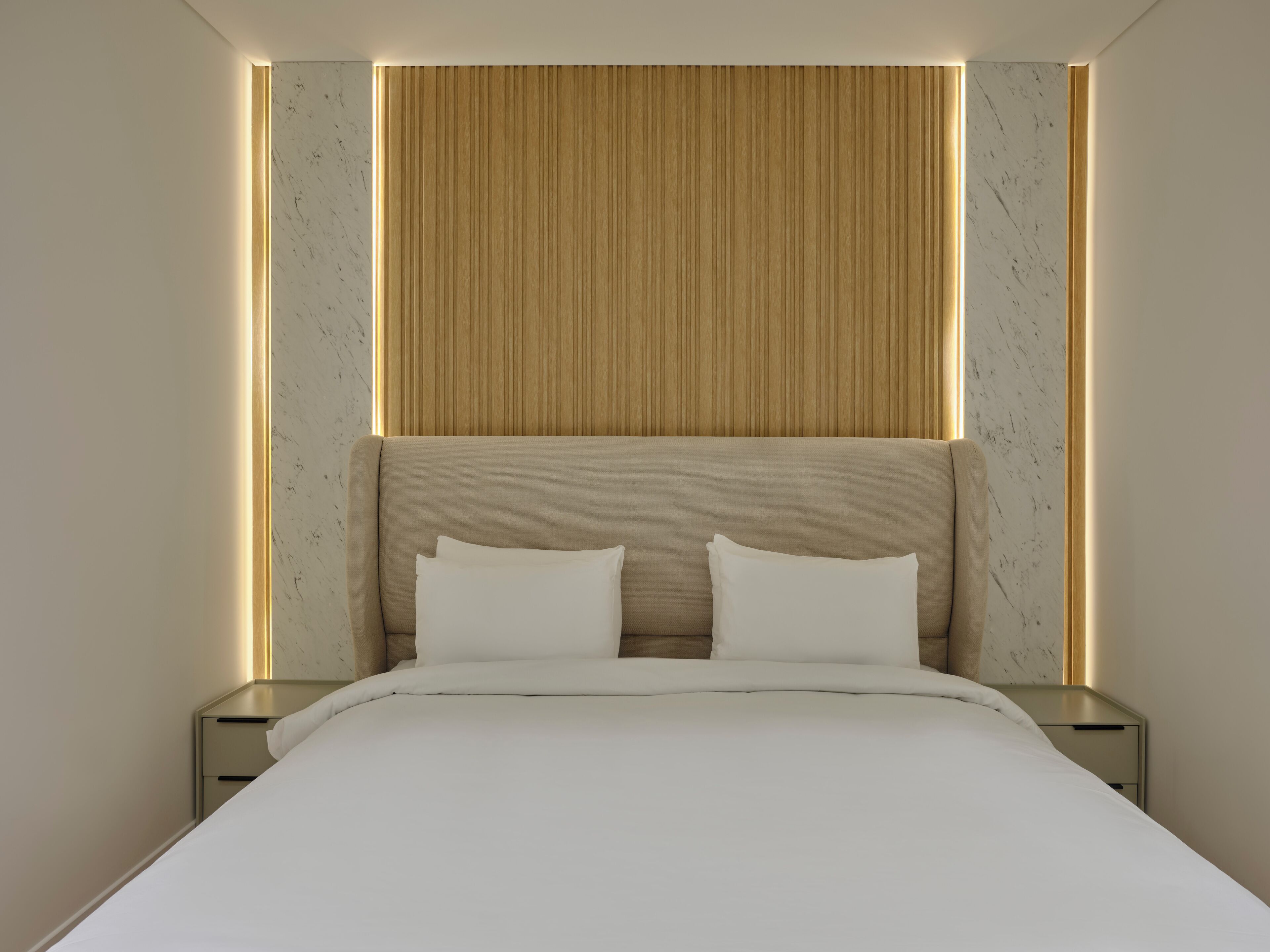 Une chambre d’hôtel moderne avec un grand lit, une tête de lit en bois et des tables de chevet.