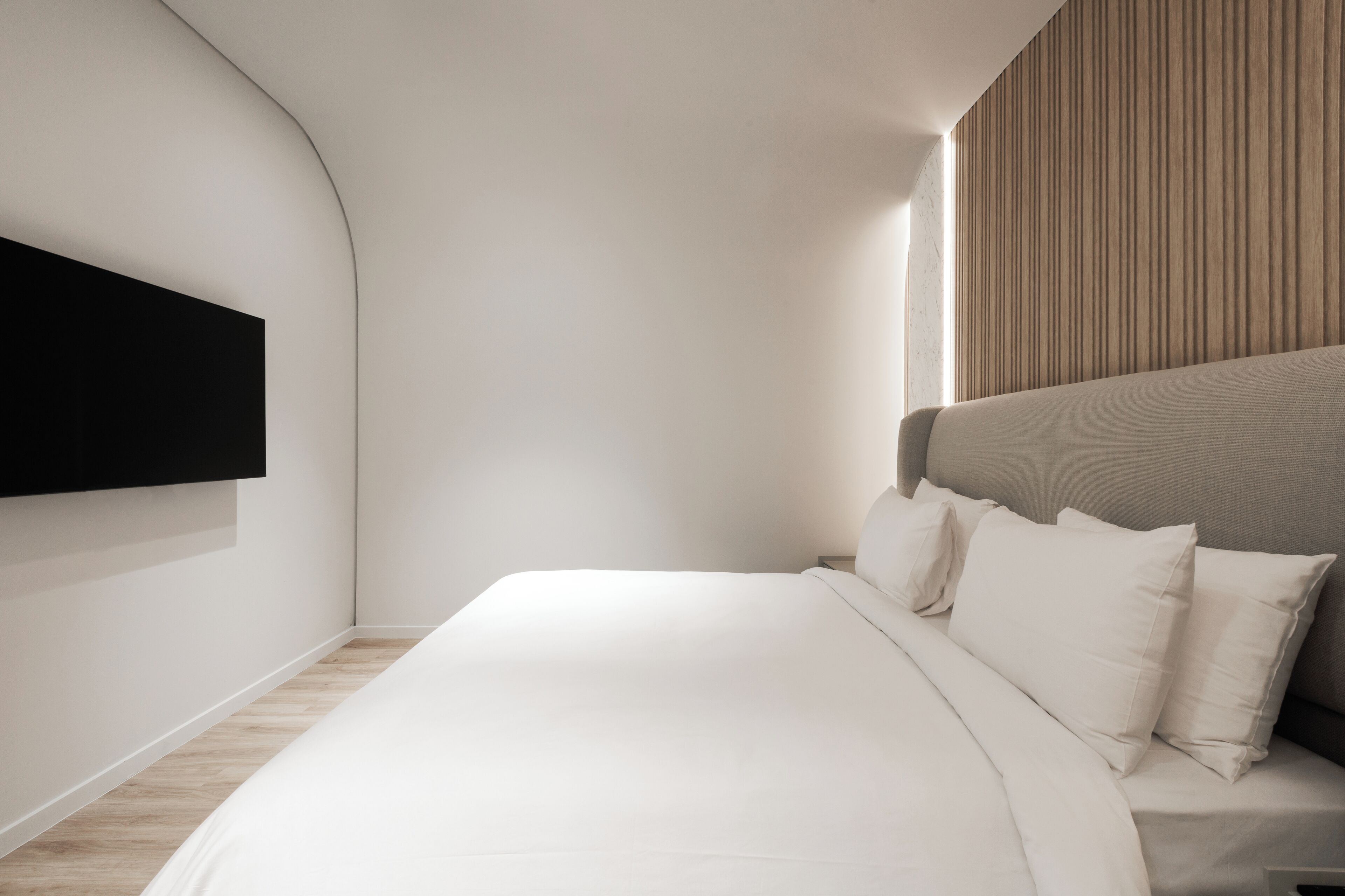 A modern bedroom with a large bed, a mounted TV, and a wooden panel wall.