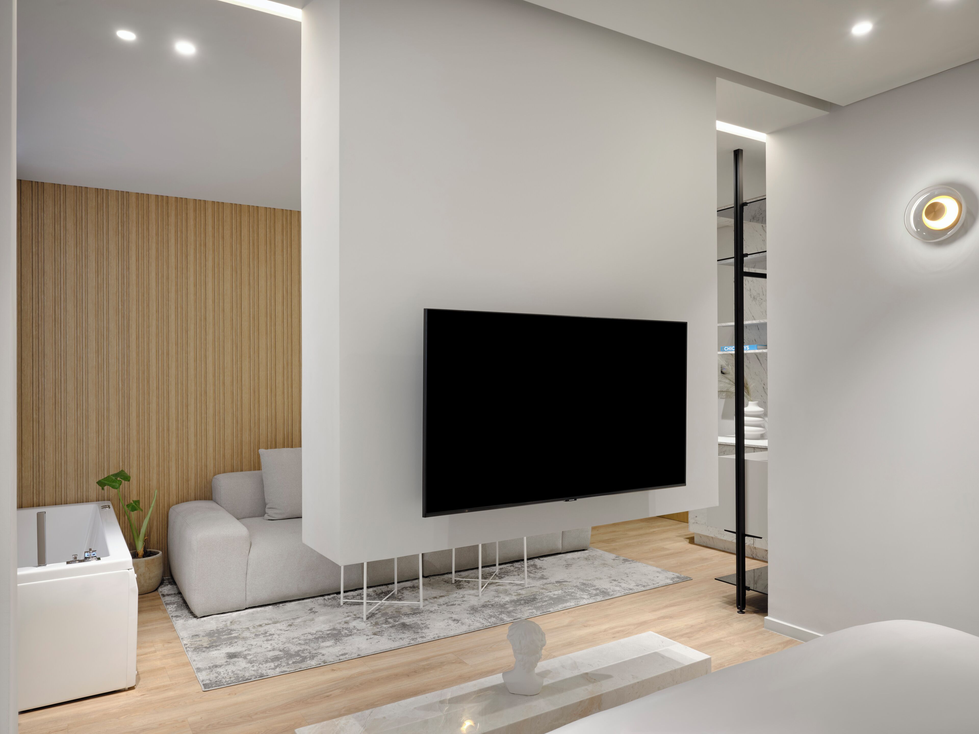 Uma sala de estar moderna com uma televisão de tela plana grande fixada na parede, um sofá, uma mesa pequena e um vaso com planta.