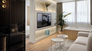 A modern living room with a flat-screen TV mounted on the wall, a potted plant, a small round table with a glass of water, and a sofa. - Nur Aparthotel Athens (Athens)