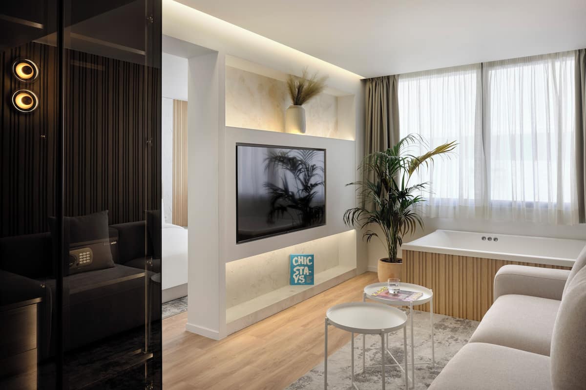 A modern living room with a flat-screen TV mounted on the wall, a potted plant, a small round table with a glass of water, and a sofa.