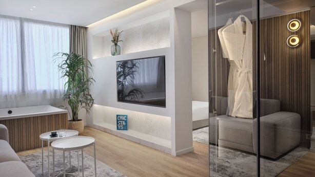 A modern living room with a flat-screen TV, a glass shower enclosure, a seating area with a sofa, and a small table. - Nur Aparthotel Athens (Athens)
