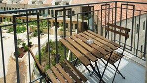 Ein Balkon mit Holztisch und -stühlen mit Blick auf einen Innenhof, im Hintergrund Gebäude und Baustellen.