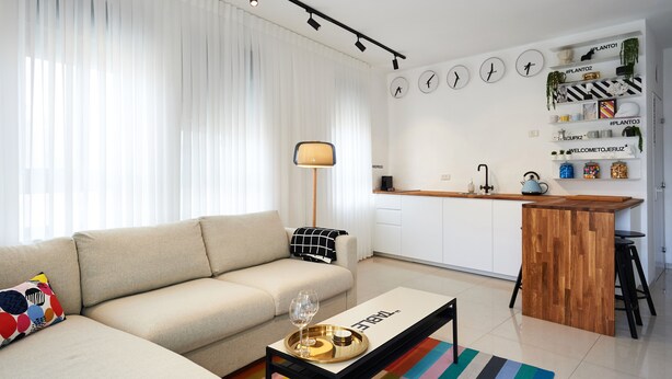 Ein modernes Wohnzimmer mit einer Couch, einem Couchtisch mit Tablett und einem farbenfrohen Teppich.