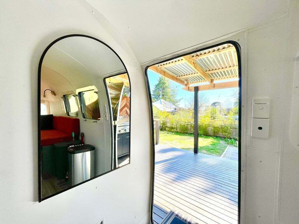 A compact RV interior with a mirrored wall, a small seating area, and a grill outside.