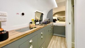 Un baño moderno con tocador, lavamanos y espejo. Hay una ventana pequeña y una puerta que da a un dormitorio.