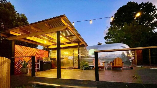 Un área de estar al aire libre con techo, un banco de madera, un vehículo y un edificio con pared de patrón espiga.