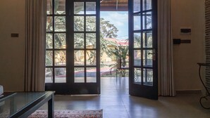 A room with a large glass door leading to an outdoor area with a view of trees and a building. - Villa Naya (Kampot)