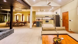 A modern kitchen with a dining area, a sofa, and a wooden table with fruit. - Villa Naya (Kampot)