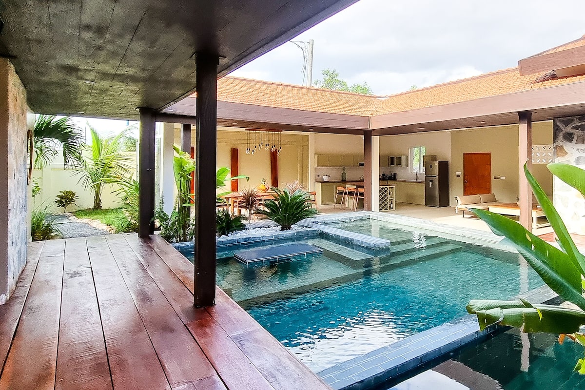 Une maison moderne dotée d’une piscine, d’un patio couvert et d’une cuisine visible à travers une porte ouverte.