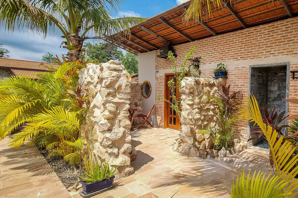Un bâtiment en briques avec un mur en pierre, une porte en bois et un patio carrelé agrémenté de plantes tropicales.