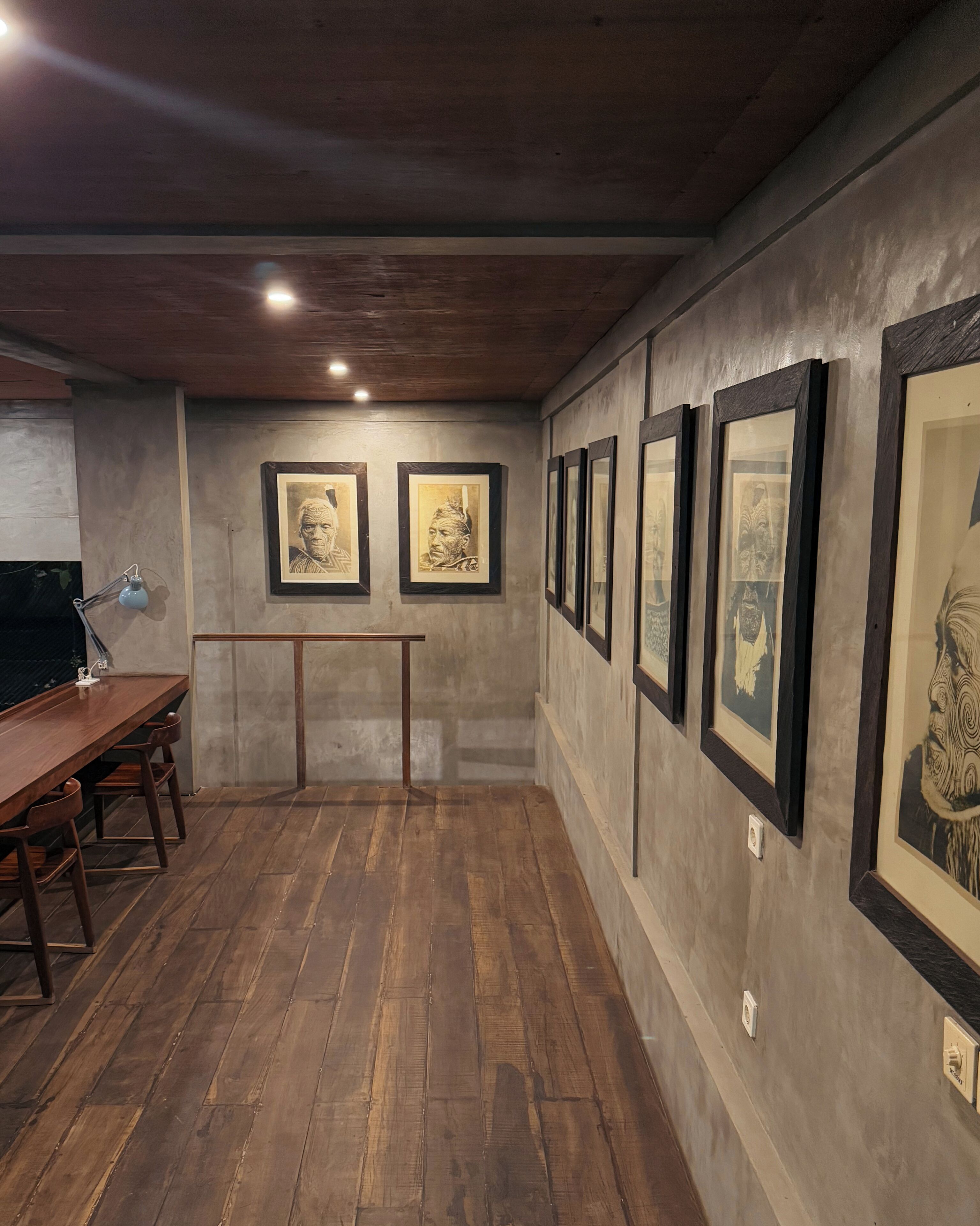 Una galleria con opere d'arte incorniciate alle pareti, un tavolo di legno con sedie e un pavimento in cemento.
