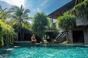 A man sitting by a pool with a staircase and lounge chairs in the background. - Mangroove Bay Boutique Hostel (Pemuteran)