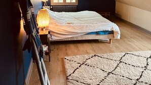 Ett sovrum med ett sluttande tak, en säng, ett fönster, en lampa och en matta.