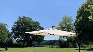 En utomhusplats för picknick med ett bord och en bänk, ett stort parasoll och en gräsyta med träd i bakgrunden.