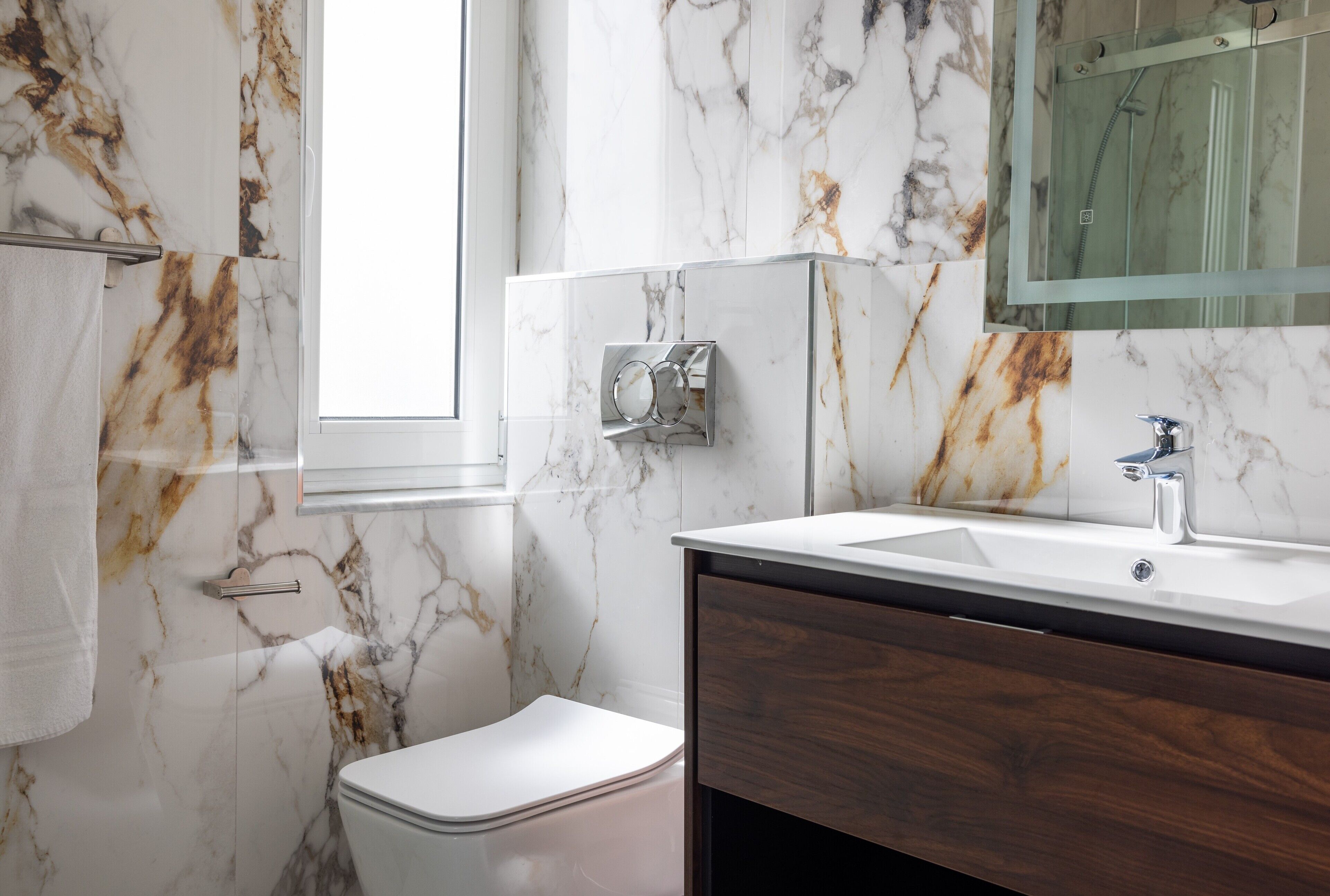 Ein Badezimmer mit Marmorwand, Toilette in Weiß, Holzwaschtisch mit Waschbecken und einer Duschkabine aus Glas.