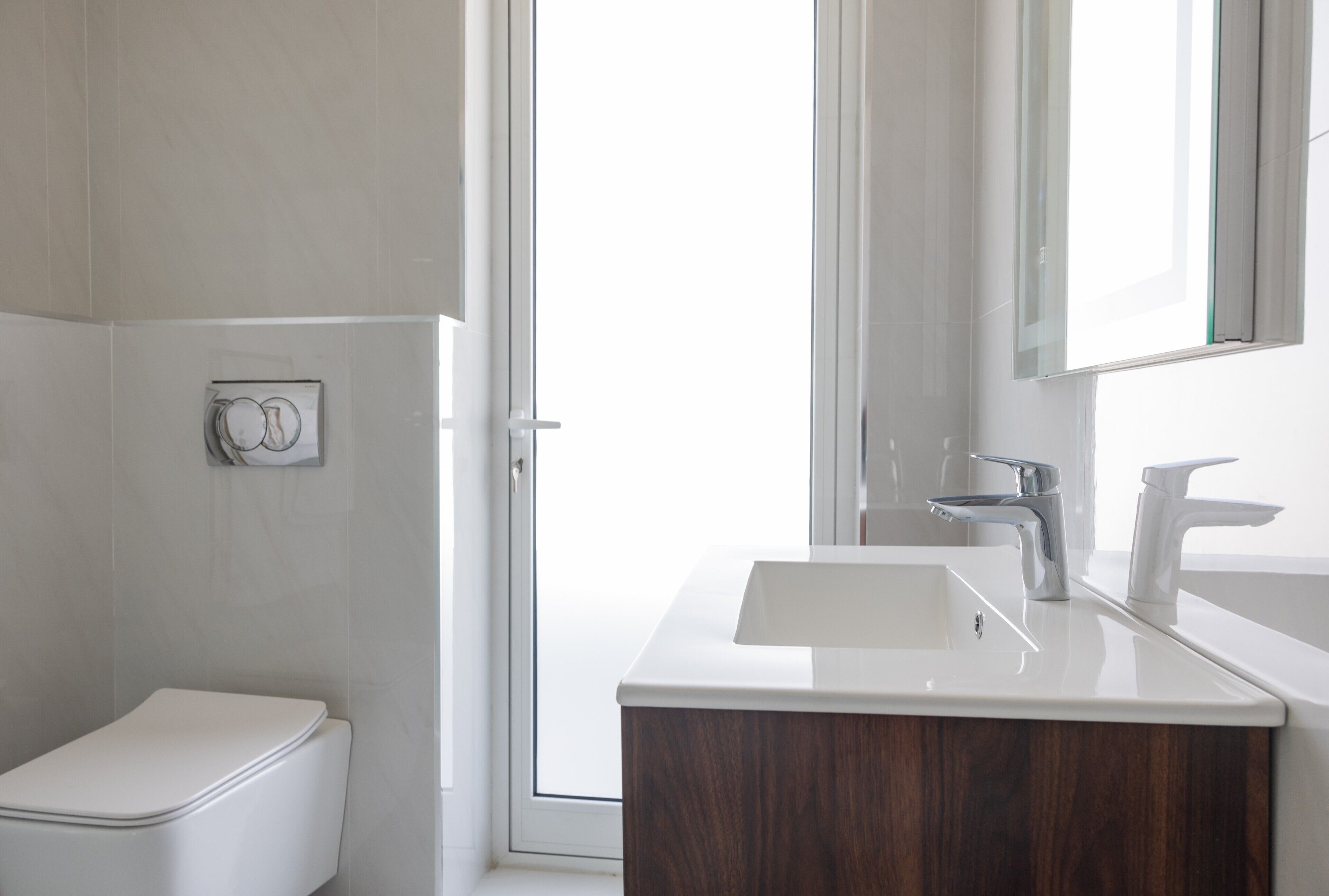 Une salle de bain moderne avec des toilettes blanches, un meuble-lavabo en bois, un lavabo blanc et un grand miroir.