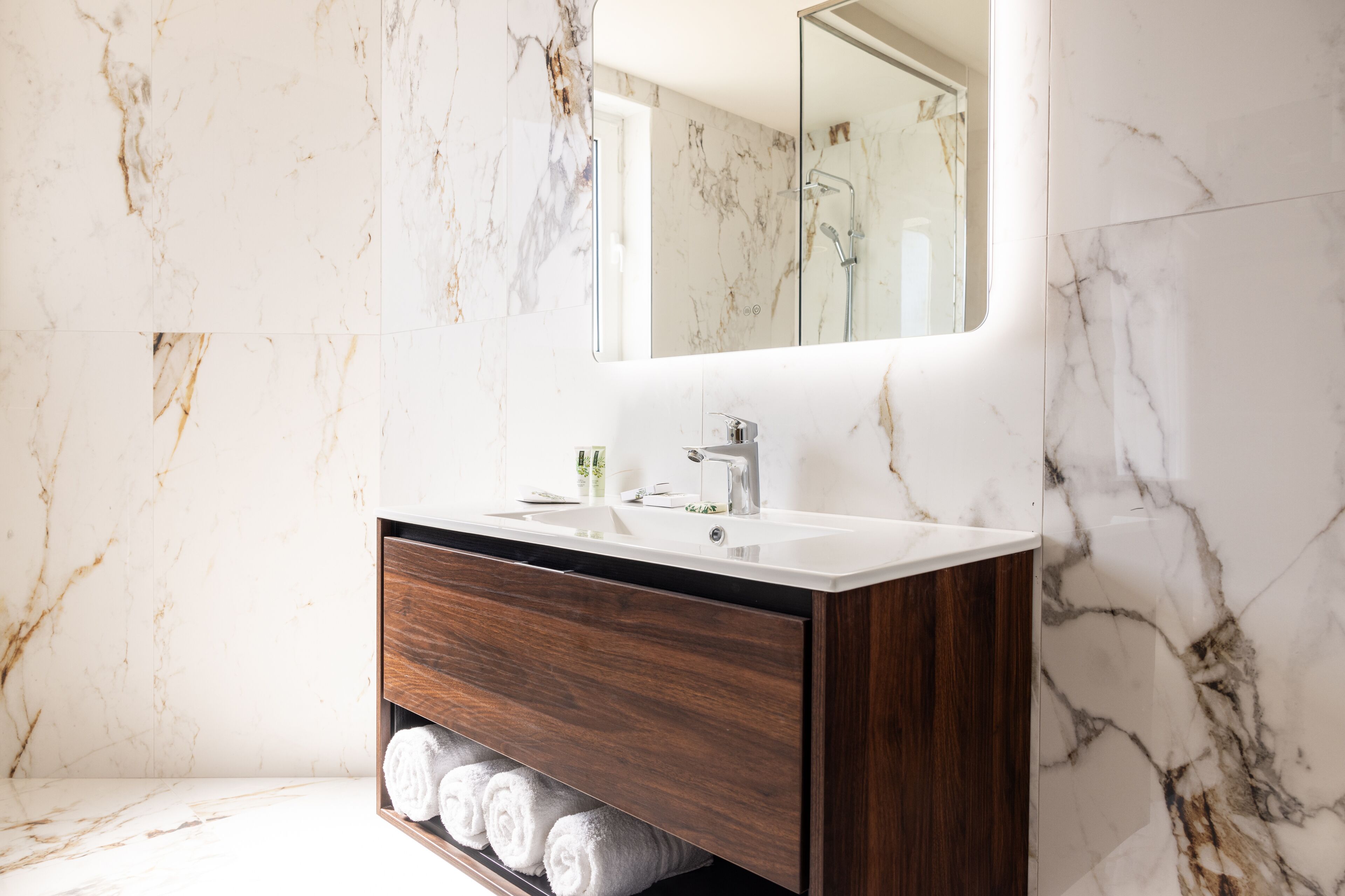 Une salle de bain avec un mur en marbre, un meuble-lavabo en bois, un lavabo et un miroir.