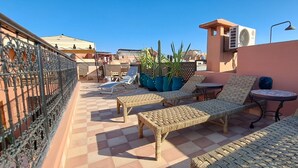 A rooftop terrace with wicker furniture, potted plants, and an air conditioning unit. - Riad parfum d'orient (Marrakech)