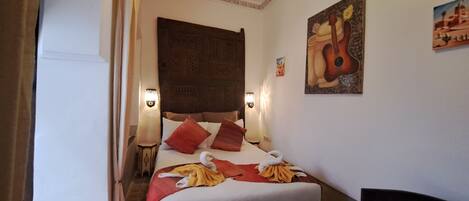 A hotel room with a large bed, a headboard, wall-mounted lights, and artwork.
