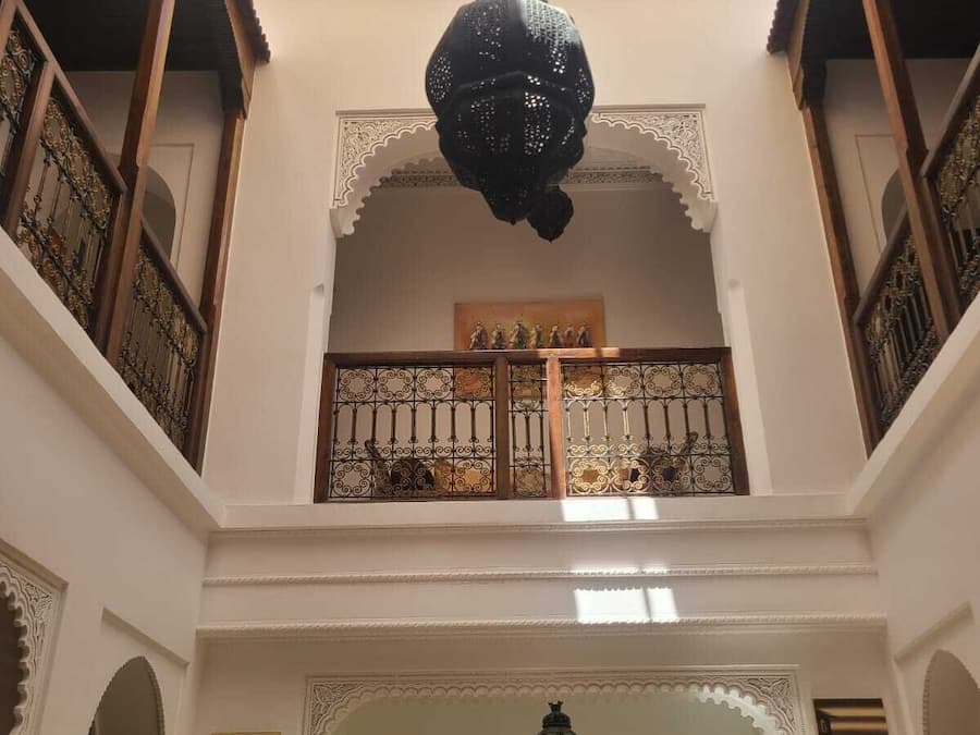 A multi-level interior with ornate railings, a central chandelier, and a decorative archway.