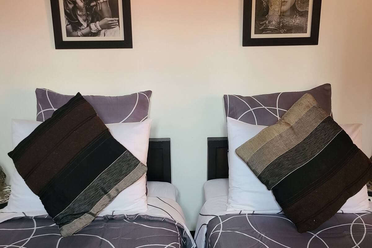A double bed with patterned bedding and two pillows, a framed picture above the bed, and a plain wall.