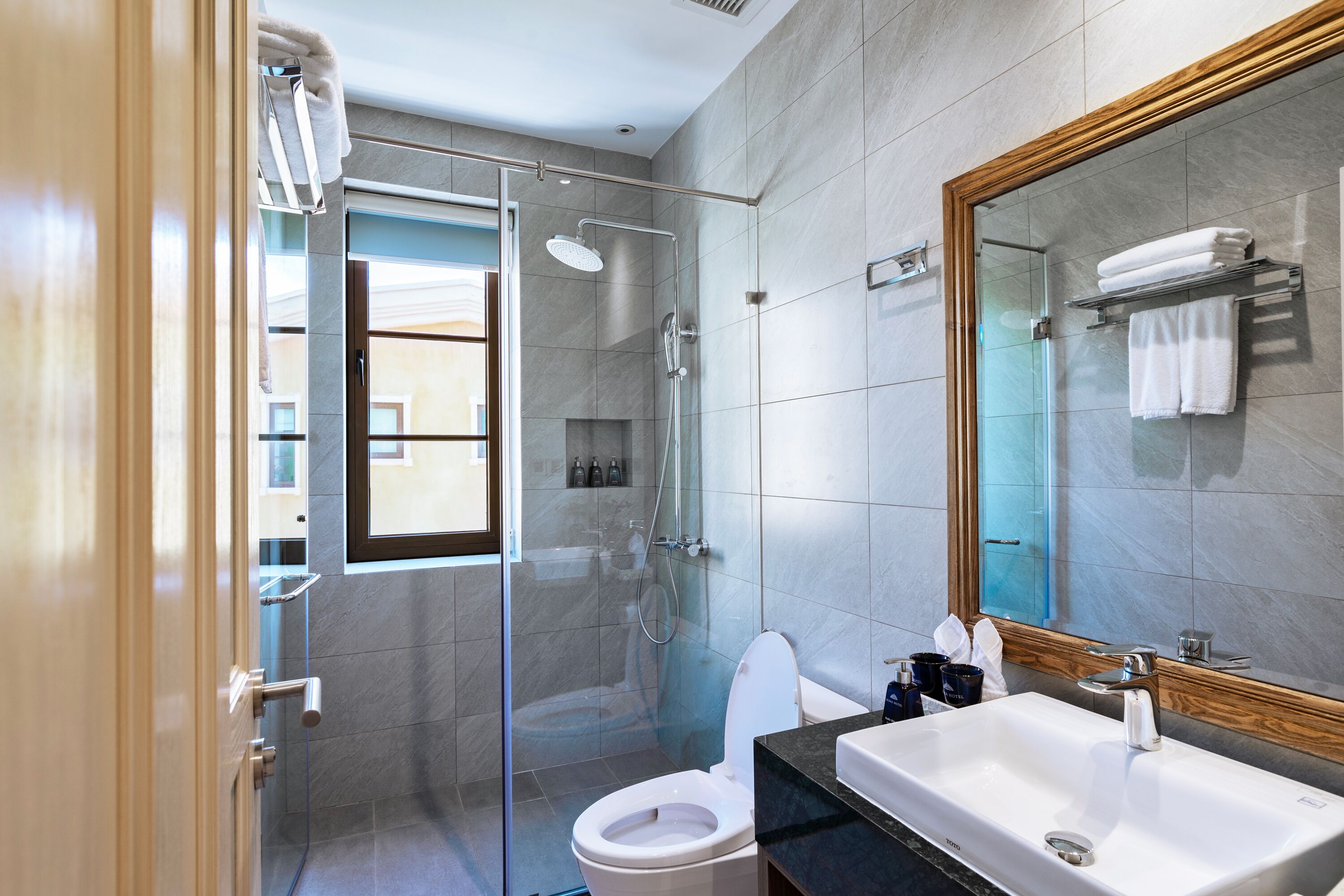 Un baño moderno con ducha envuelta en vidrio, inodoro blanco y un espejo grande sobre el lavamanos.