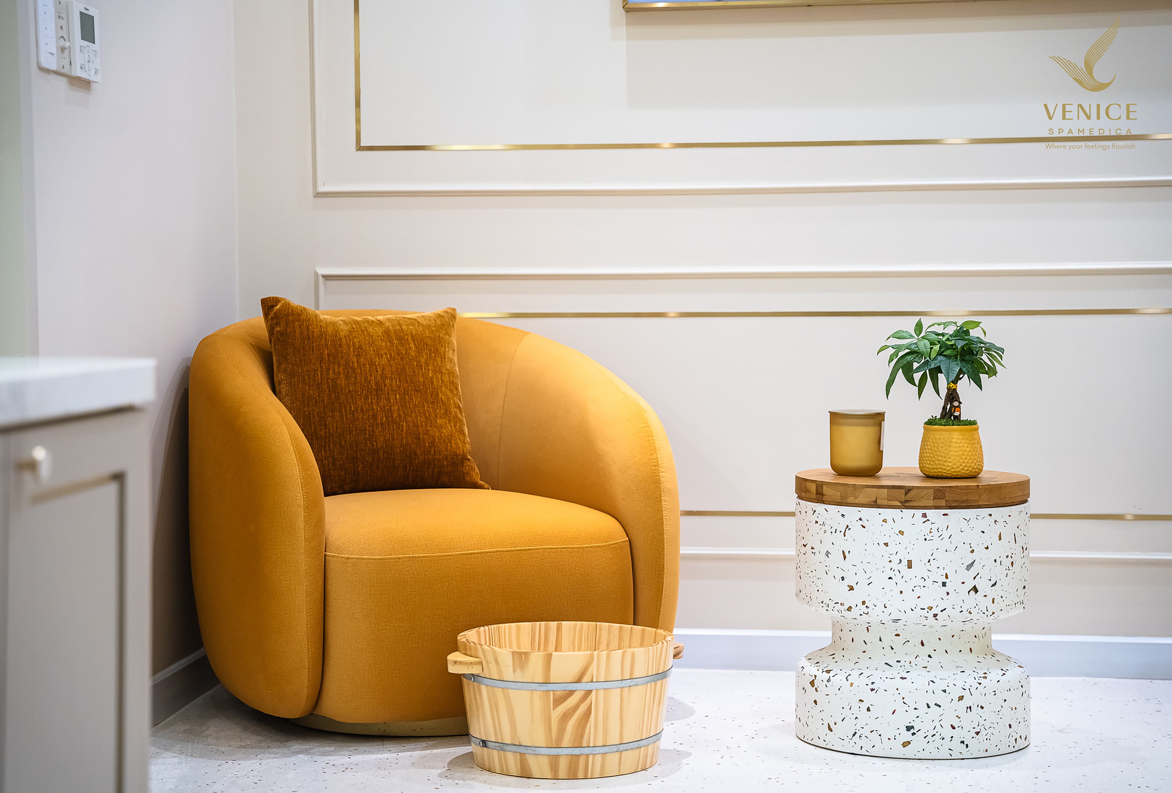 Una habitación moderna con un sillón color mostaza, una pequeña mesa redonda con una planta y un cubo de madera.
