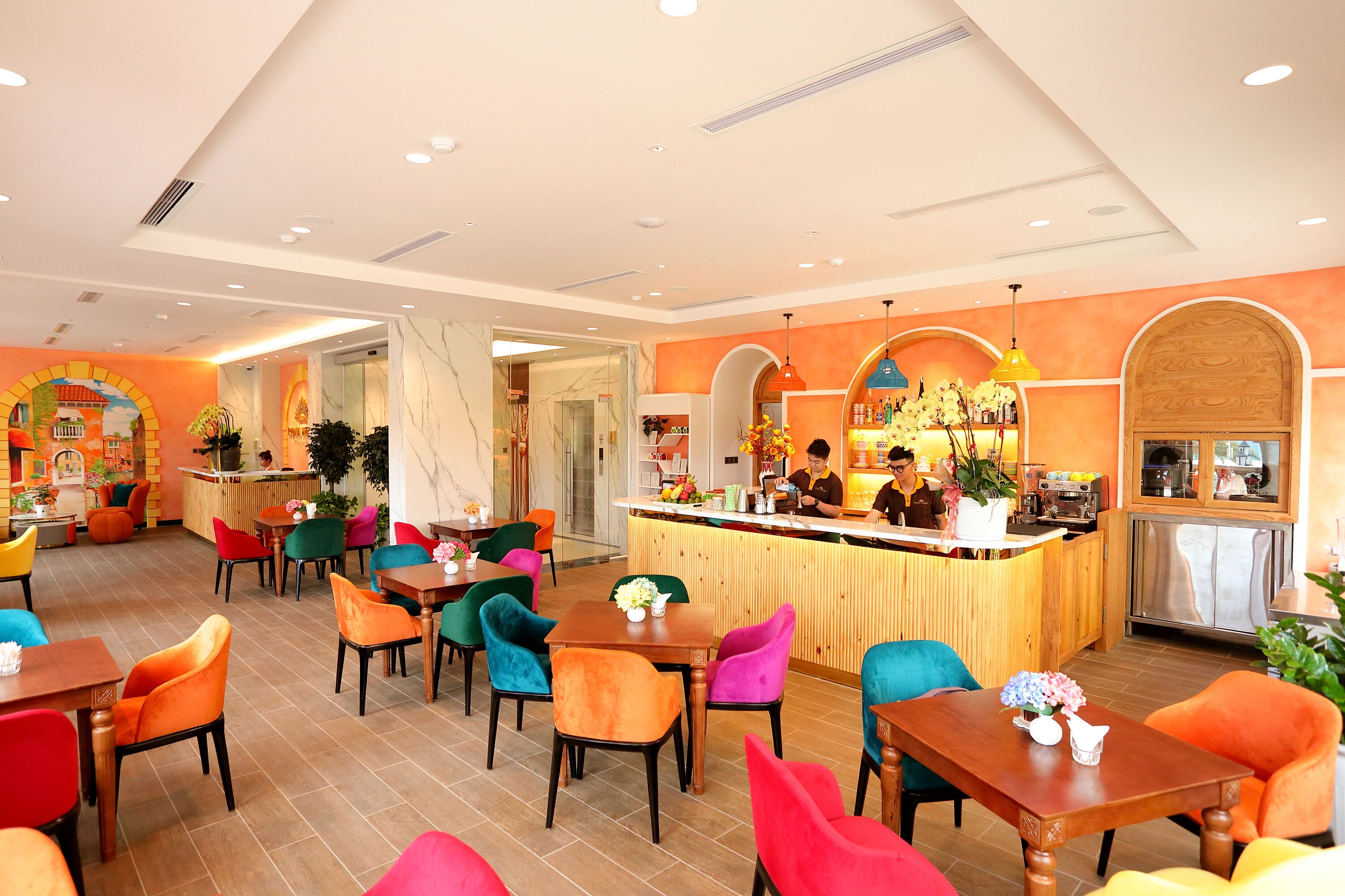 A restaurant with a wooden counter, colorful chairs, and a kitchen area.