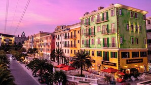 A street with colorful buildings, including a hotel named "ROMA COFFEE" with outdoor seating and a red umbrella.